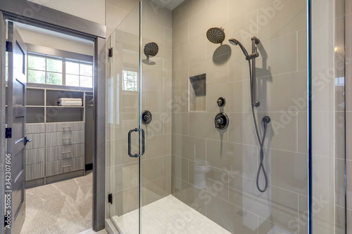 Natural new classic slick bathroom interior with new glass walk in shower  white tub and walk in closet.