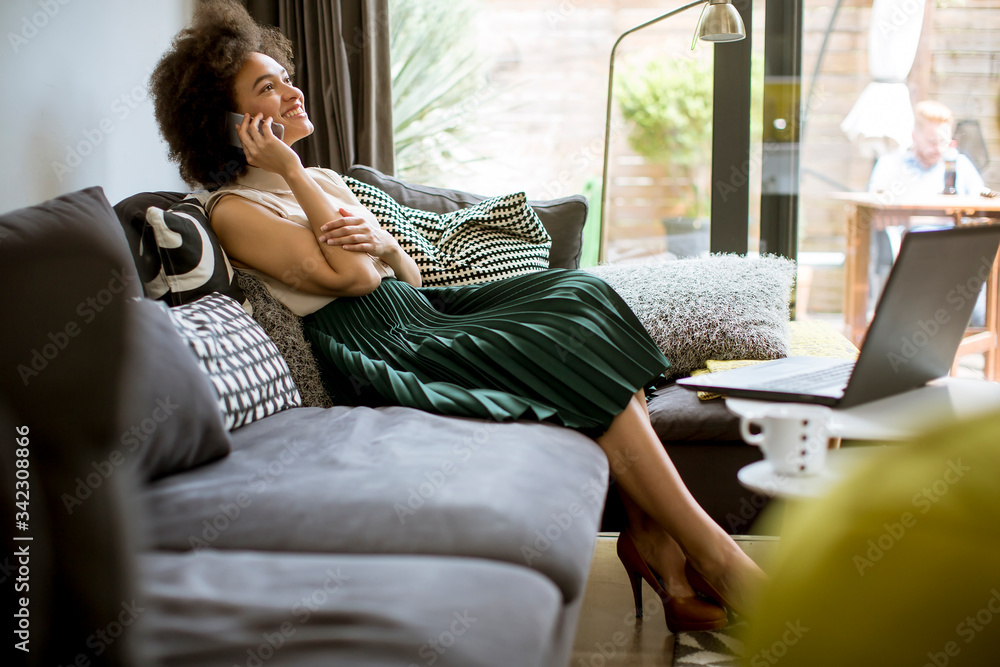 Fototapeta premium Young curly hair african woman relaxing at home and using mobile phone