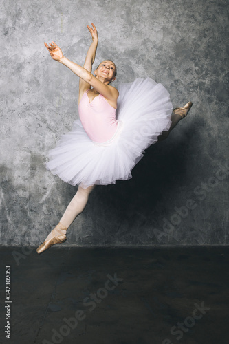 Fototapeta Naklejka Na Ścianę i Meble -  Pretty young ballerina dancer dancing classical ballet against rustic wall