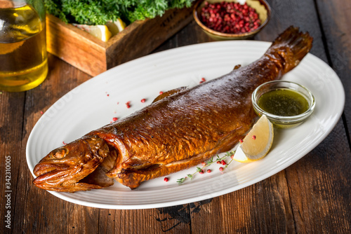 Smoked trout served with sauce, lemon on a white plate