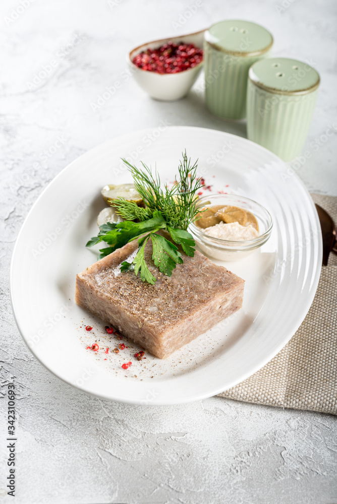 Jellied meat with fresh herbs and mustard on a white plate