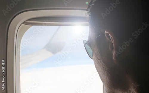 Young passenger looking out through window of the flying airplane. Side view of handsome man against plane window sitting and looking out. Wanderlust. Lonesome traveler and dreamer. Travel concept.