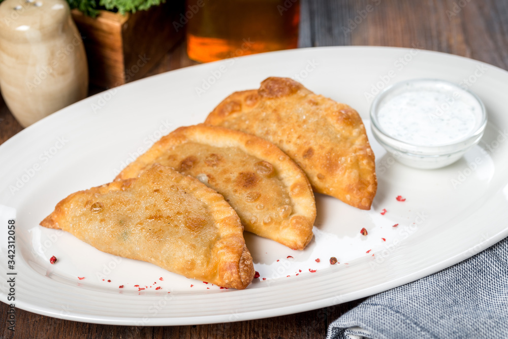 Three pasties on a white plate with sour cream