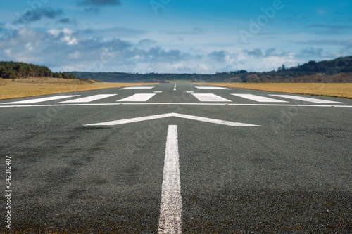 Small airport asphalt runway with markings for landings. Blue cloudy sky and fields around. Nobody. photo