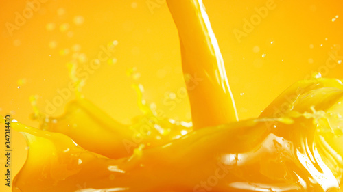 Fotografia Orange juice splash on coloured background