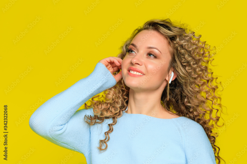 beautiful woman portrait with  curly hair on yellow  background posing  and listen music wiith earphones  - Image