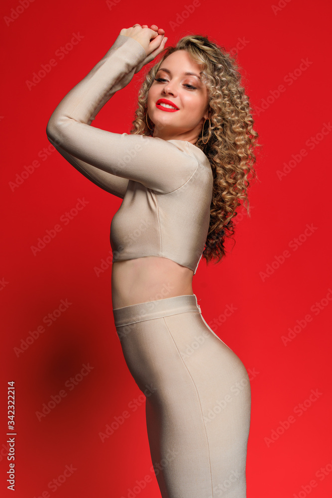 beautiful young woman  in beige clothes  and with curl hair posing  on red   background - Image