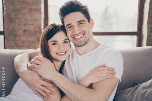Portrait of her she his he nice attractive lovely affectionate cheerful cheery gentle couple sitting on divan embracing honey moon at modern industrial loft style brick interior living-room flat