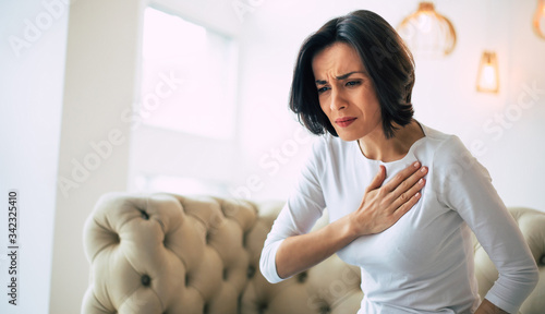 Pressure in the chest. Close-up photo of a stressed woman who is suffering from a chest pain and touching her heart area. photo