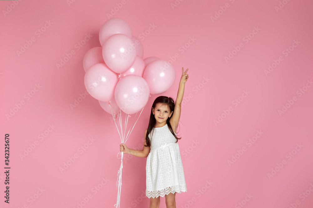 Smiling adorable little child girl with pastel pink air balloons showing victory gesture isolated over pink background. Beautiful happy kid on a birthday party. space for text Smiling adorable little child girl with pastel pink air balloons showing victory gesture isolated over pink background. Beautiful happy kid on a birthday party. space for text