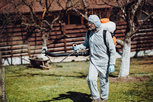 worker wearing protective clothing and spraying pesticides, insecticides and other organic chemicals using mistblower machine photo