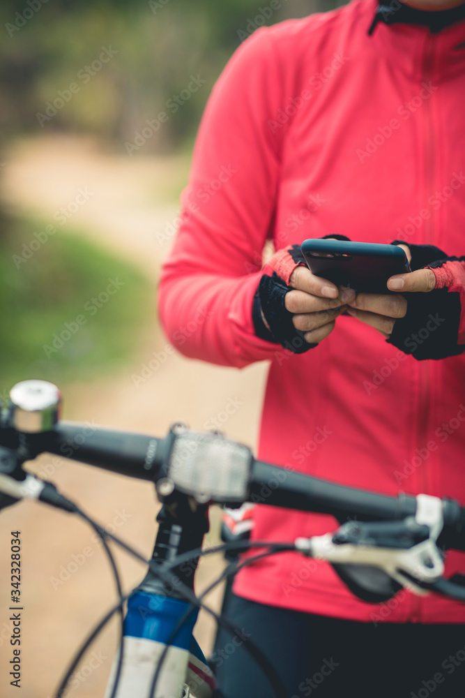 Cyclist use smartphone for navigation when riding mountain bike on forest trail Cyclist use smartphone for navigation when riding mountain bike on forest trail