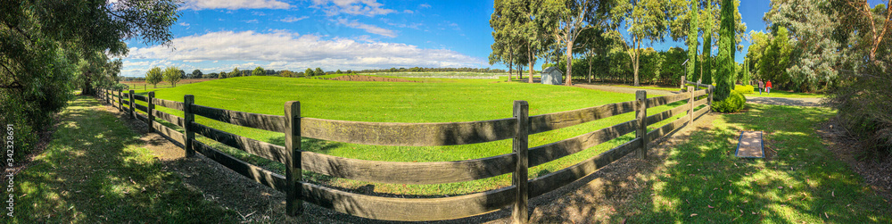 WIde panorama of wooden fence and grassland undre blue skies in Australia