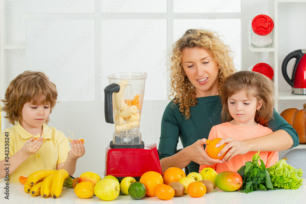 Mother with children making smoothie in a white kitchen. Family mother and child daughter and son blended smoothie with healthy fruits ingredients. Detox smoothie and healthy food.