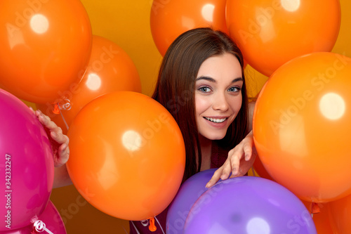 Smiling caucasian girl posing with bright color air balloons on yellow background. Beautiful happy young woman on a birthday holiday. close-up © producer