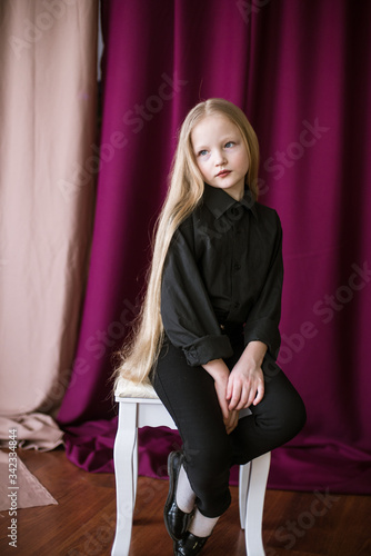 Cute little girl with long blond hair in a black shirt and jeans on a red background in the studio