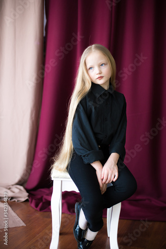 Cute little girl with long blond hair in a black shirt and jeans on a red background in the studio