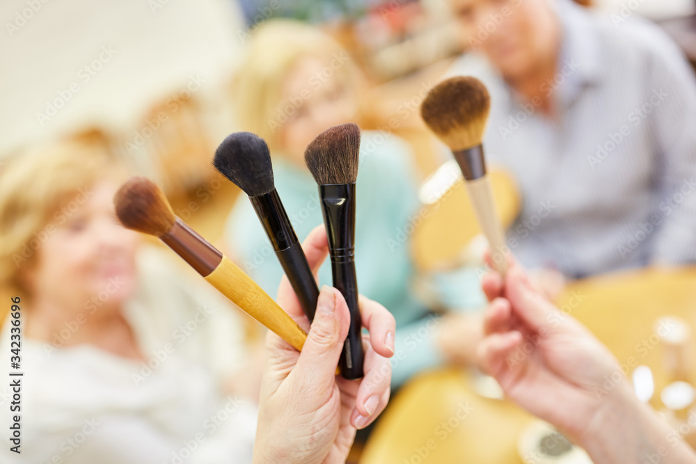 Visagist zeigt Schminkpinsel für das altersgerechte Make-Up im Senioren Schminkkurs - obrazy, fototapety, plakaty 