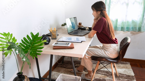 Attractive young beautiful asian woman Entrepreneur or freelancer working at home with laptop business reports and online communications on living room sofa, working remotely access concept. © snowing12