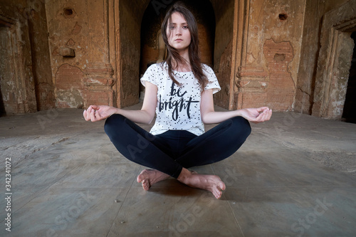 A beautiful girl is meditating in lotus position, sitting on the floor in front of a Buddha statue in an ancient temple in Bagan in Myanmar. photo