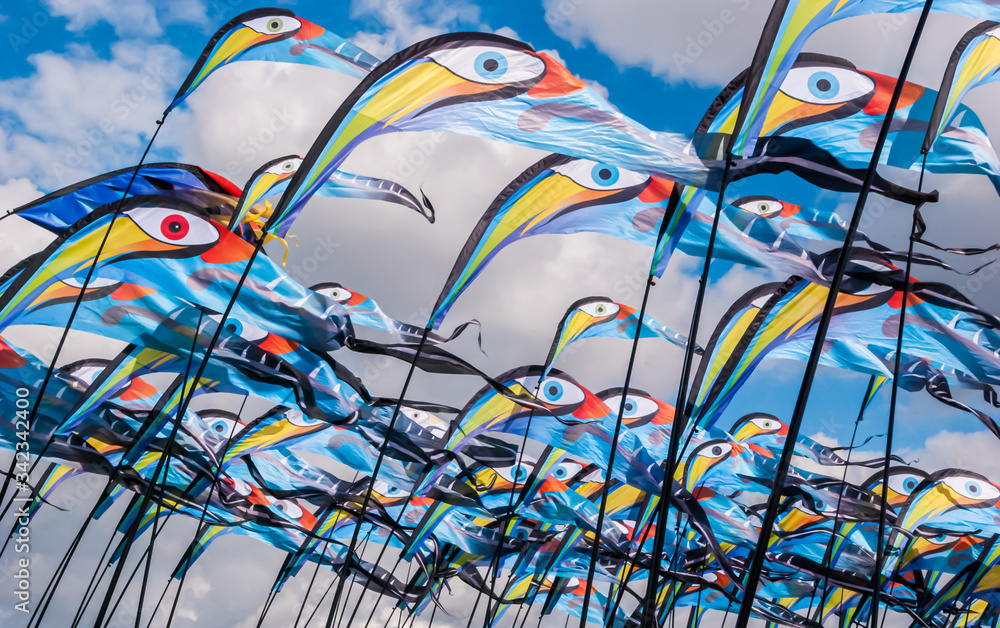 Colorful and bright bird flag kites on poles with a blue sky and clouds in the background at Southsea Kite Festival, Portsmouth, UK