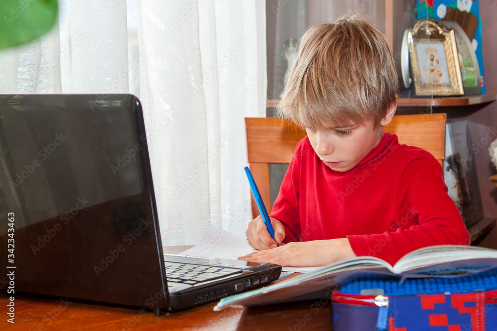 School kid in self isolation using laptop for homework, Social Distance learning online education during coronavirus epidemic. Cute boy studies and does school homework at home during quarantine School kid in self isolation using laptop for homework, Social Distance learning online education during coronavirus epidemic. Cute boy studies and does school homework at home during quarantine