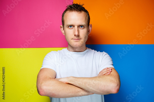 Portrait of a young, cheerful guy on a multi-colored background, dressed in a white T-shirt, creates a fashionable hairstyle, positive emotions