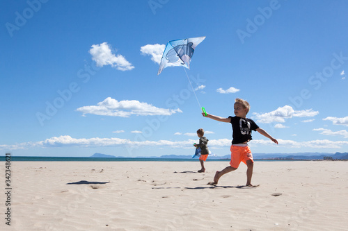 Happy boys running on the beach in summer with a kite. Beautiful sea and sand