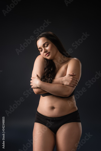 Front view of plus size girl enjoying and hugging her body on black background © LIGHTFIELD STUDIOS