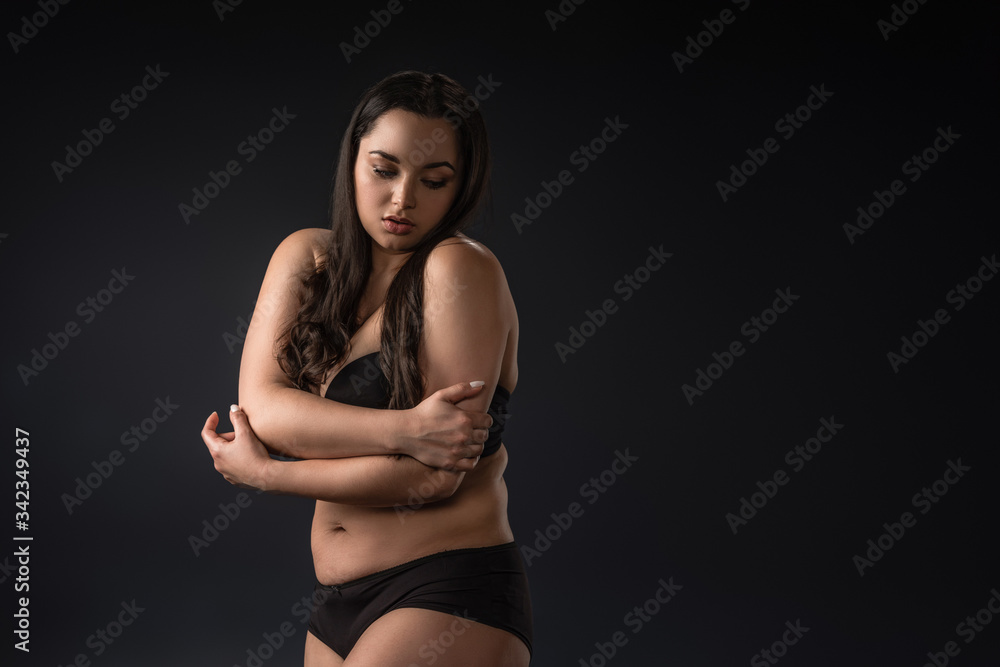 Shy plus size girl in underwear covering body with hands on black background