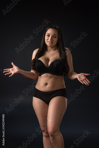 Smiling plus size girl in underwear with outstretched hands on black background