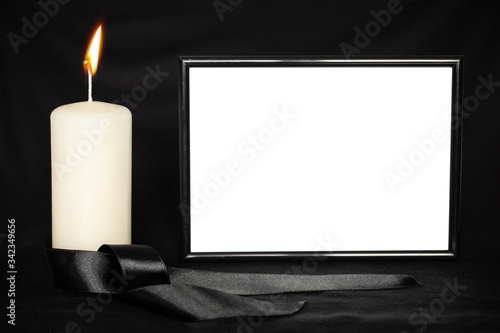 A burning white candle, a mourning ribbon, and a black frame with space for text on a black background photo