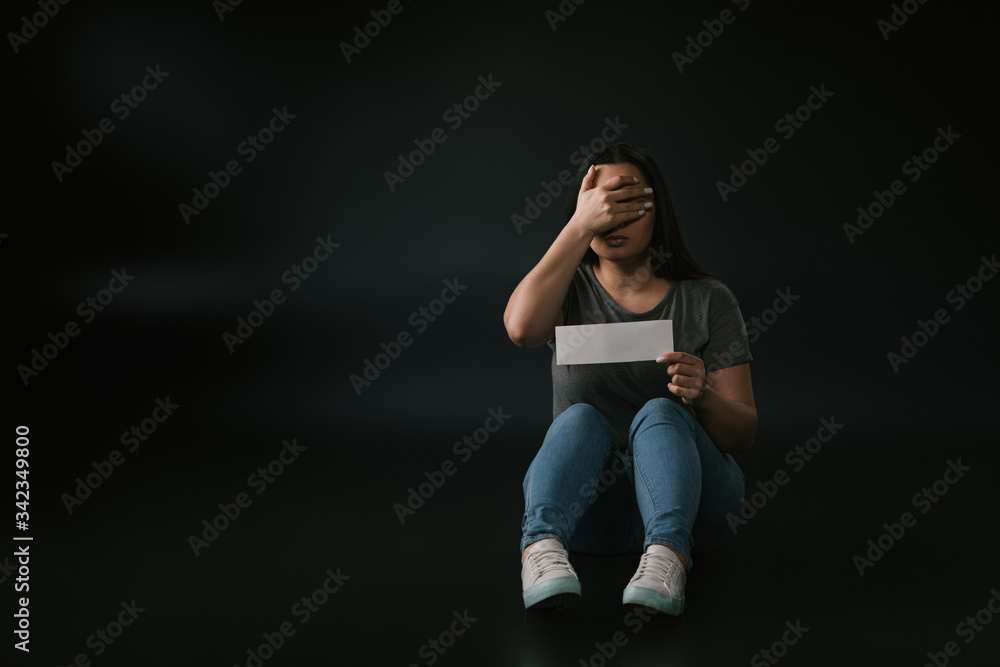 Front view of plus size girl with facepalm gesture and empty card in hand on black background