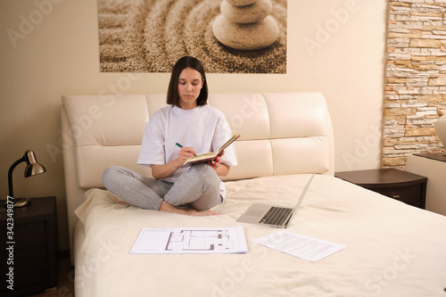 Young  woman businessman on self-isolation during a coronovirus pandemic COVID-19 on self-isolation works at home, sits on bed, checks mail, does his work remotely, telework