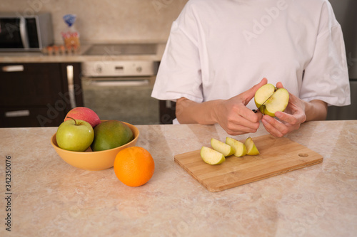 Unrecognizable female hands in the kitchen cuts fresh fruits, prepares to make fresh, smoothie, on self-isolation during the coronovirus pandemic covid-19, close-up