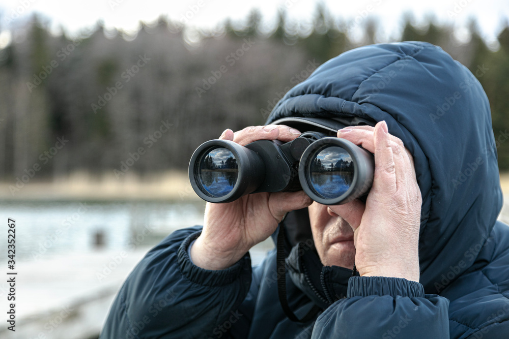 A man on the riverbank is looking through binoculars