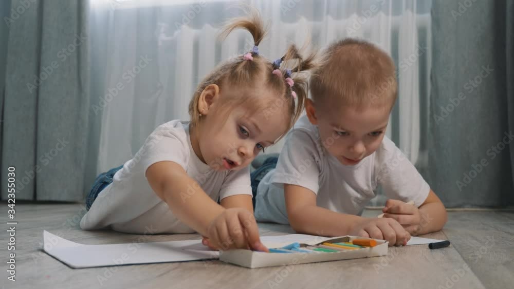 Cute children draw with crayons on white paper lying on the floor in the room. Cute children draw with crayons on white paper lying on the floor in the room.