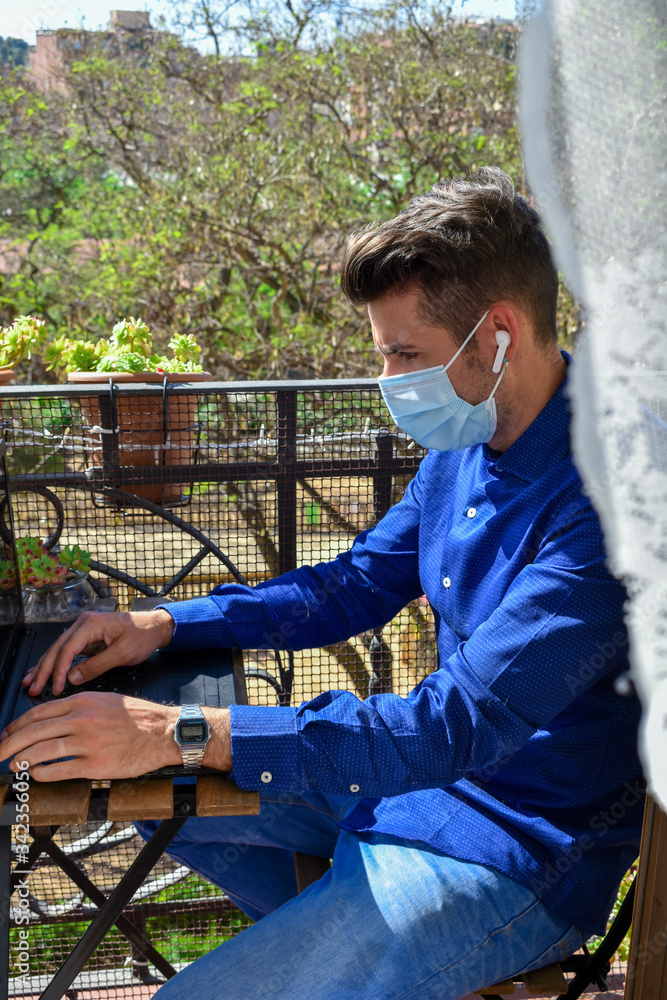 Obraz premium Man wearing a face mask making a video call with the laptop on his balcony, confined at home by the quarantine due to covid-19