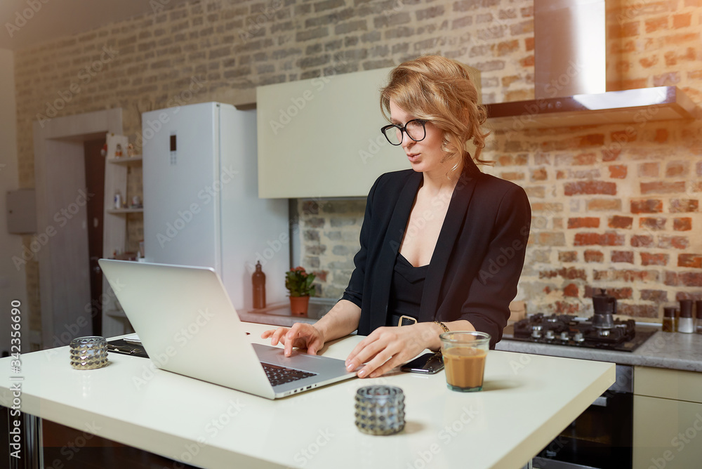 A woman in glasses works remotely on a laptop in her kitchen. A girl searching for news on the internet at home. A lady preparing for a lecture on a video call.