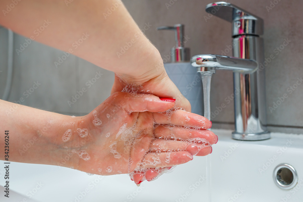 White sink with a silver faucet in the bathroom. Gray can with liquid soap for hands. Turning on the tap water, personal hand hygiene. Hand washing under running water White sink with a silver faucet in the bathroom. Gray can with liquid soap for hands. Turning on the tap water, personal hand hygiene. Hand washing under running water