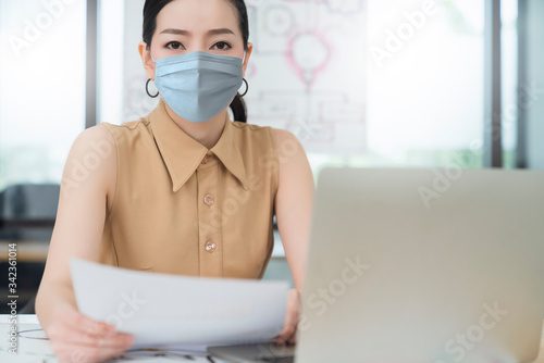 sick and worry asian female manager wearing protection mask from covid 19 coronavirus spread epidemic working in office with stress emotion face expression office background