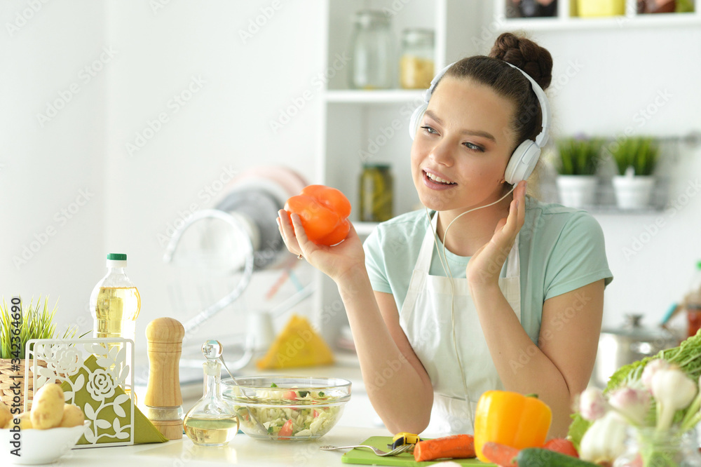 Beautiful young woman making salad and listening to music