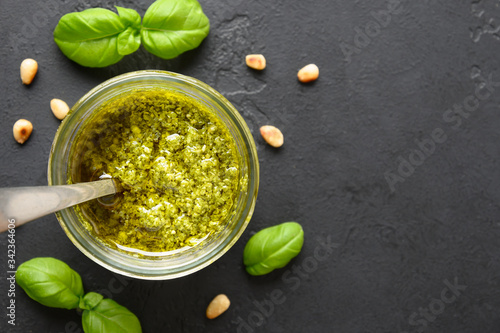 Pesto sauce in glass jar with basil leaves and nuts. View from above.