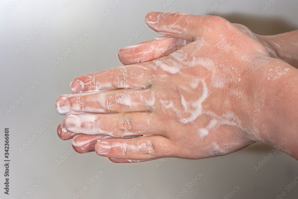 Hands of a young guy in soap foam on a grey background. Hand washing. Minimal hygiene, virus protection concept. Hands of a young guy in soap foam on a grey background. Hand washing. Minimal hygiene, virus protection concept.