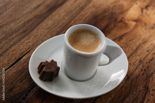 A cup of espresso with a chocolate candy maple leaf shaped on wooden background
