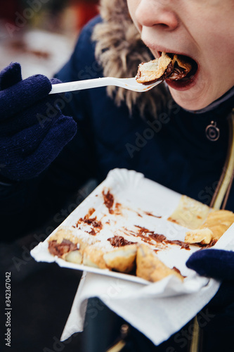 Young girl enjoying freshly prepared crepes which are thin pancakes with chocolate spread filling outside at Christmas market. Popular warm street food in Switzerland especially in winter time. 