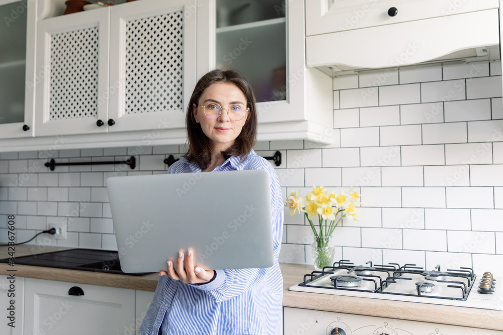 Portrait Shot of a Beautiful Smiling Young Woman Working on a Laptop at Her Desk in the Cozy Living Room. Girl Posing, Hands on Chin, Laughing Charmingly on Camera. Portrait Shot of a Beautiful Smiling Young Woman Working on a Laptop at Her Desk in the Cozy Living Room. Girl Posing, Hands on Chin, Laughing Charmingly on Camera.