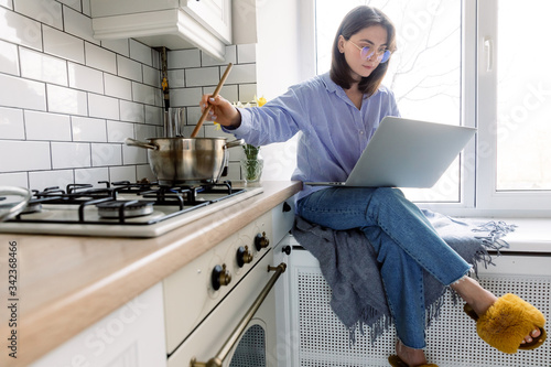 Fotografie Portrait of woman working on laptop while cooking in kitchen
