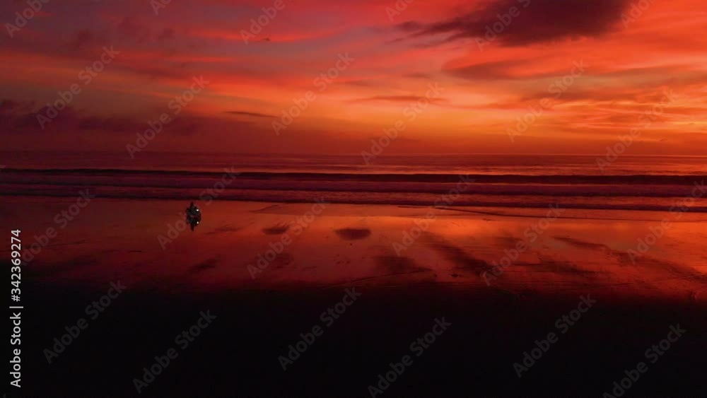 Woman riding a motorbike on beach after vibrant sunset, profile follow shot aerial Woman riding a motorbike on beach after vibrant sunset, profile follow shot aerial