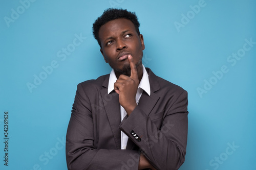 Young afrcain man in suit thinking on blue background photo